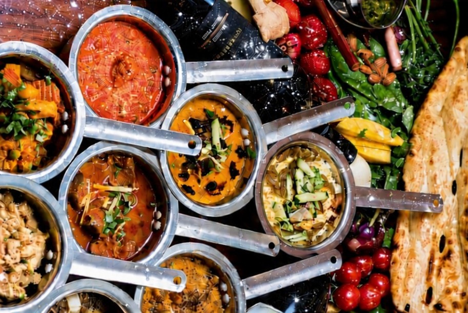 Curries in steel pans with naan, greens and fresh vegetables
